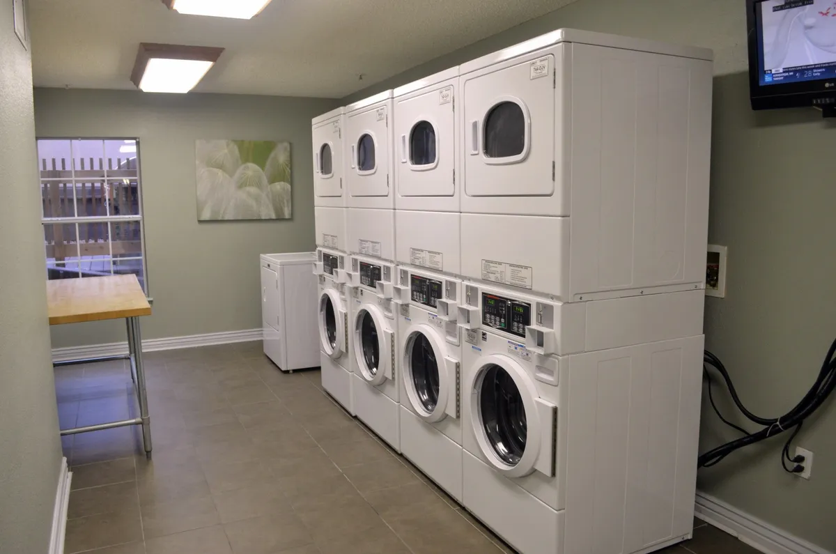 A well-organized laundry room with washing machines, dryers, a folding table, and decorative wall art. The practical, clean layout suggests convenience for extended stays, providing on-site laundry support in a welcoming environment.