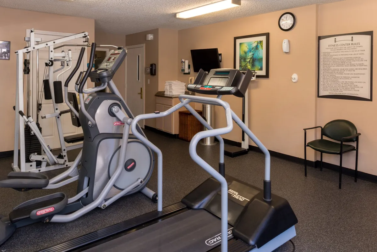 An energetic fitness center featuring treadmills, elliptical machines, a weight machine, and motivational posters. The space is bright, clean, and designed for a variety of workout routines, with appealing artwork on the wall for an inviting vibe.