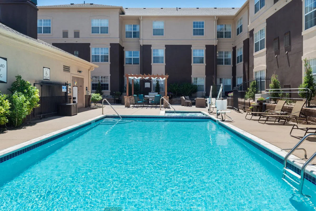 A lively outdoor pool scene complete with a spacious swimming pool, comfortable seating area, and the hotel building facade as a backdrop. Guests are seen enjoying swimming, sunbathing, and socializing in a relaxed, inviting environment.