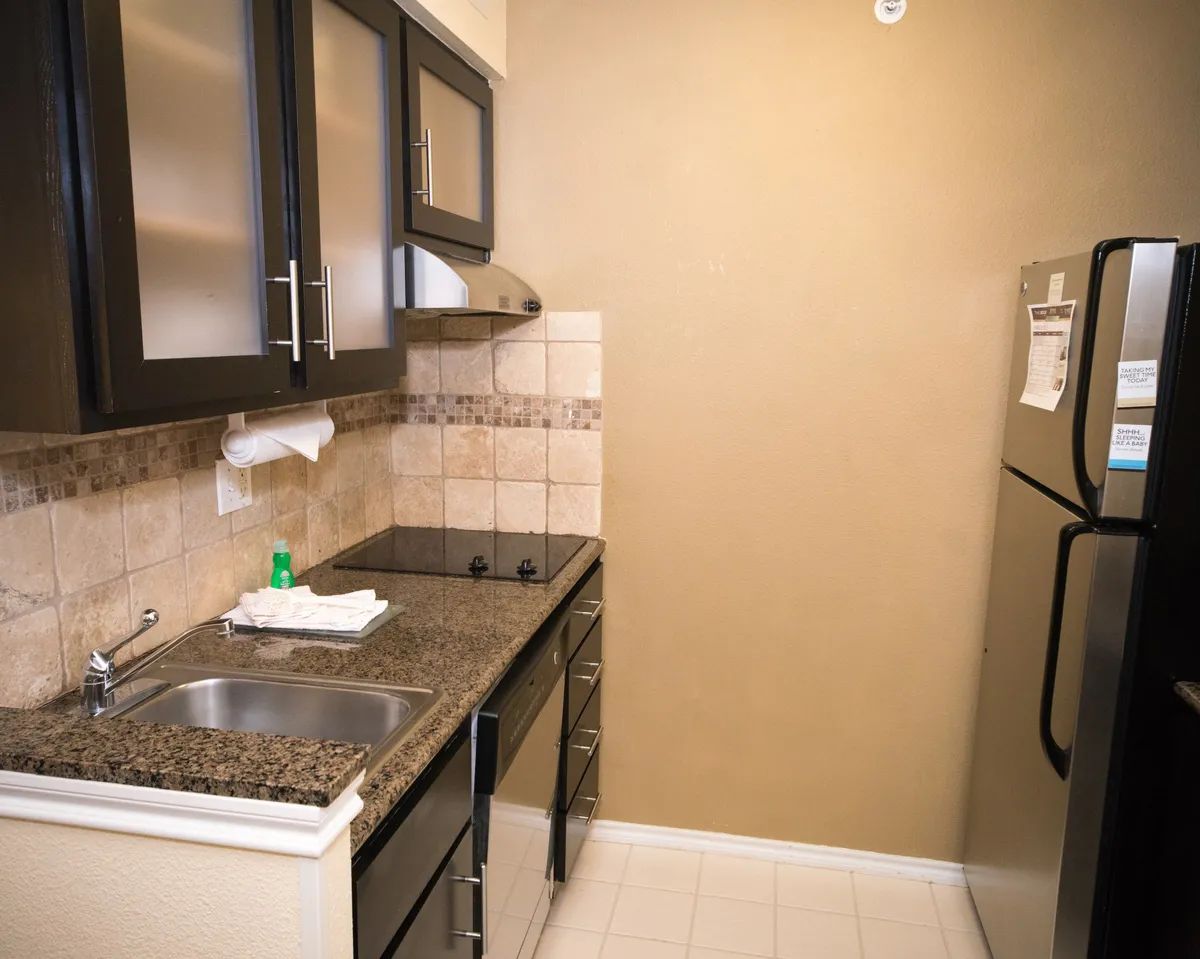 A contemporary kitchen featuring a granite countertop, stainless steel refrigerator, glass-front cabinets, and a stylish tile backsplash. The space is set for cooking and entertaining, with ample room for meal prep and storage.