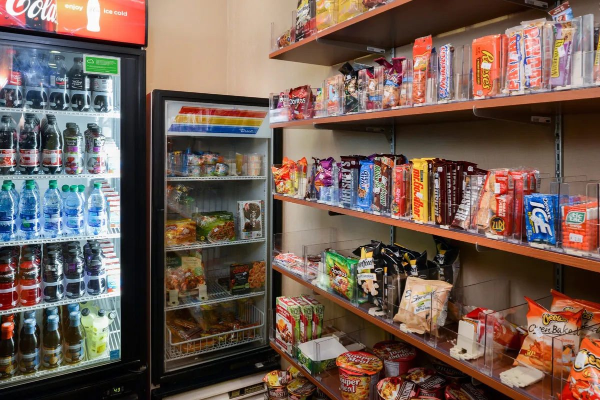 A well-lit snack area offering a refrigerated drink display and shelves stocked with a variety of packaged snacks. The scene suggests easy access to refreshments, appealing to families looking for quick bites before or after heading out for Denver adventures.