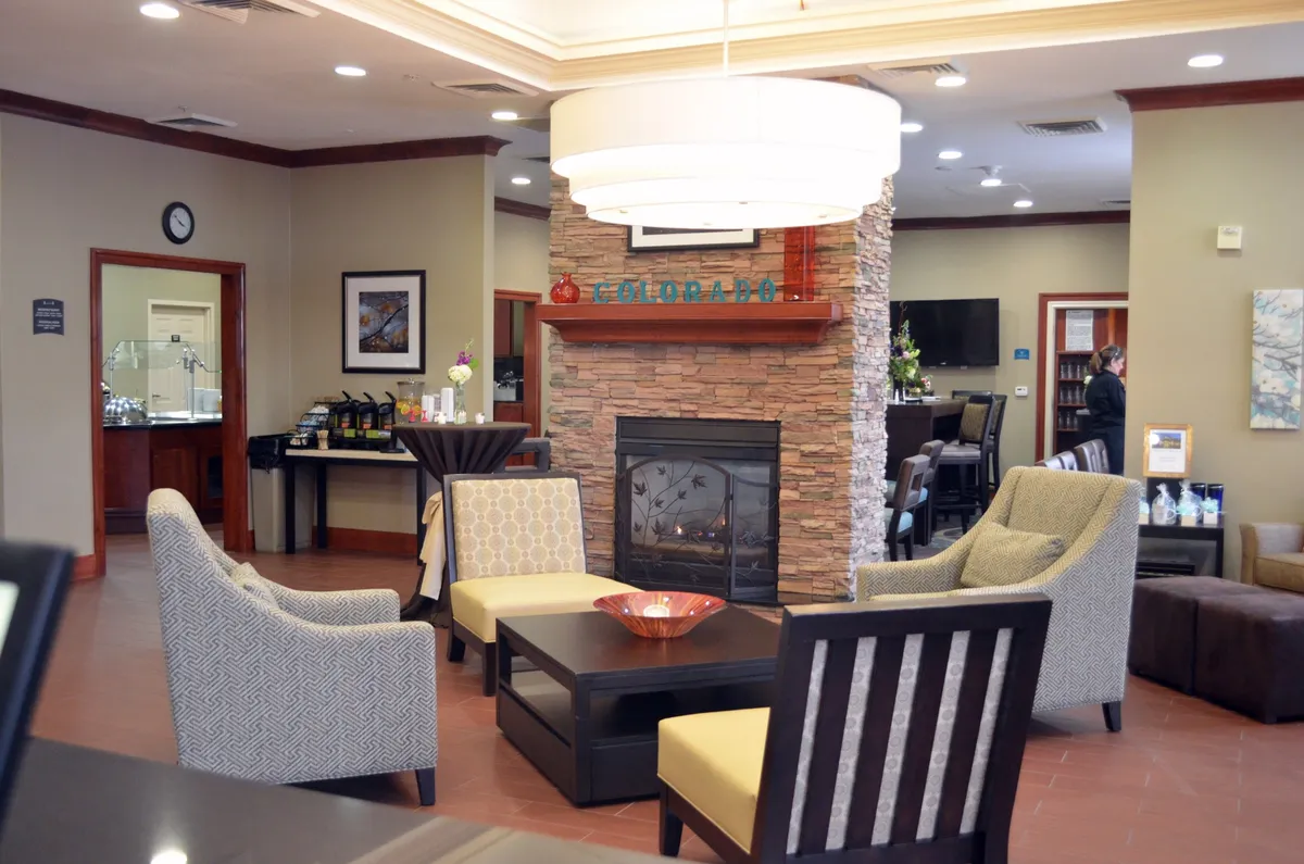This image captures a stylish living area centered around a fireplace, with a comfortable seating arrangement, a striking chandelier overhead, and tasteful decorative artwork on the walls. The space looks inviting and cozy, ideal for both relaxing and socializing, and exudes a warm, home-like atmosphere.