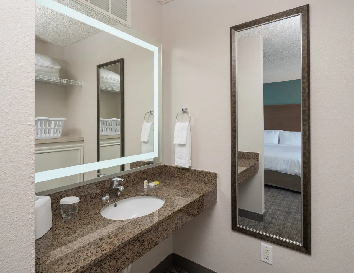 This image features a vanity area with a large mirror, granite countertop, and a modern sink, set against a mirrored wall. The space is bright, clean, and inviting, evoking a sense of relaxation and personal care.