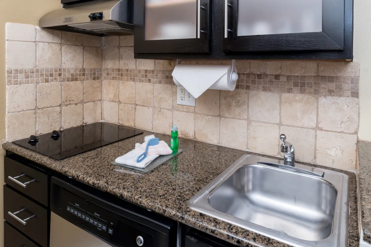 A practical and inviting kitchen scene spotlighting a granite countertop, sink, stove, and spacious kitchen cabinets. The area is ready for cooking, cleaning, and meal preparation, evoking a sense of homey comfort.